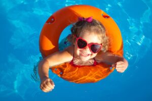 A humorous little girl is happily swimming in a pool while sporting an orange life preserver.
