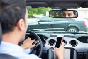 A young man wearing a blue polo shirt is driving a black car while checking his phone. Suddenly, he looks shocked, indicating he is about to have a traffic accident. 