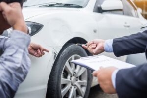 An insurance agent writes on a clipboard while inspecting a car involved in an accident, assessing and processing the claim.