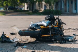 The motorcycle lies on the road following a severe collision, with significant damage visible. Close-up shows the damaged bike amidst the aftermath of the traffic accident.