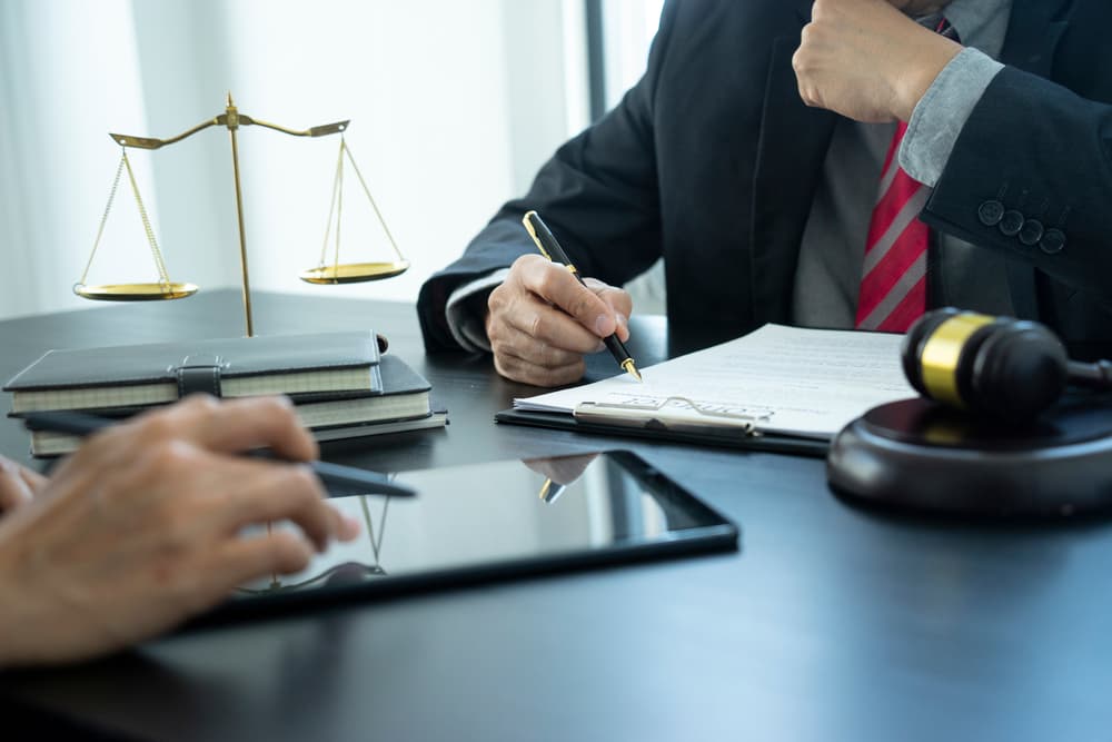 The lawyer is reviewing a draft of legal documents or contracts with a client, collaborating closely while using a tablet alongside staff or the client.