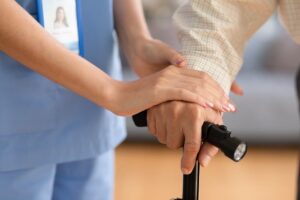 Close-up of a doctor or nurse's hand holding the hand of an elderly patient resting on a cane or walking stick, offering hope and encouragement to walk again.