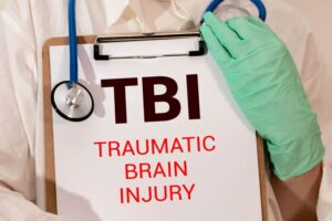 TBI (Traumatic Brain Injury) concept with the words "TBI Traumatic Brain Injury" written on a white note, placed on a background of dollar bills.