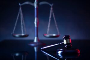 Judge's gavel, scales of justice, and Lady Justice statue under a red light—symbolizing law, order, and social justice.