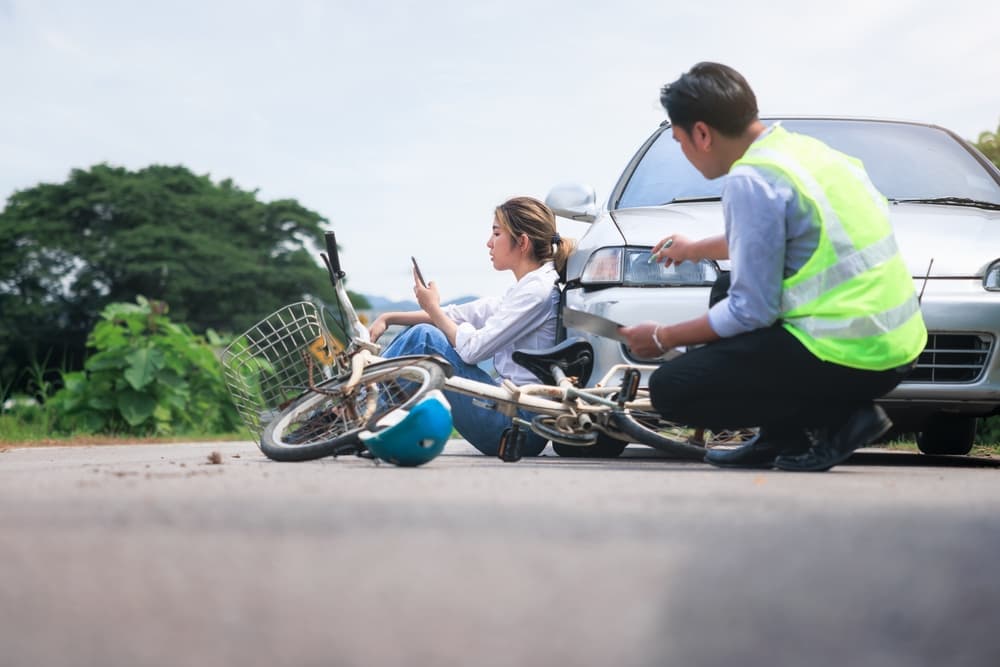 A car and bicycle collision on the road, with an injured rider and an insurance officer assisting.