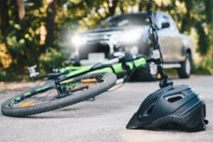 A cycling helmet lies on the asphalt beside a fallen bicycle after a car accident, symbolizing road safety and collision impact.