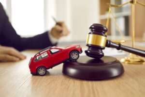 A small car model on a wooden desk beside a judge's gavel, symbolizing car accidents, legal disputes, justice, and lawyer services.