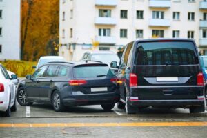 Car accident in tight parking lot, black sedan hitting parked van while backing up, reverse parking. 