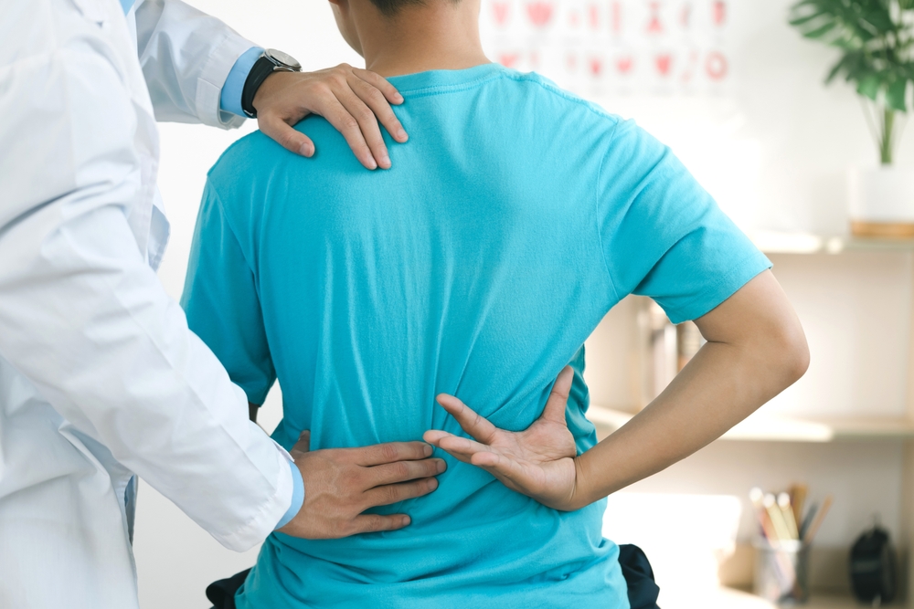 Doctor and physiotherapist treating a patient’s lower back pain in a hospital, providing massages and therapy for back injury recovery